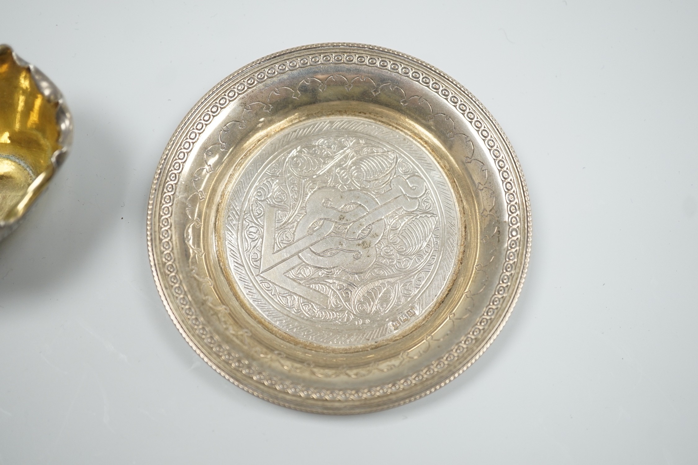 A late Victorian novelty parcel gilt silver salt modelled as a basket, with aesthetic engraved decoration, London, 1884, length 65mm, together with an Egyptian white metal small dish.